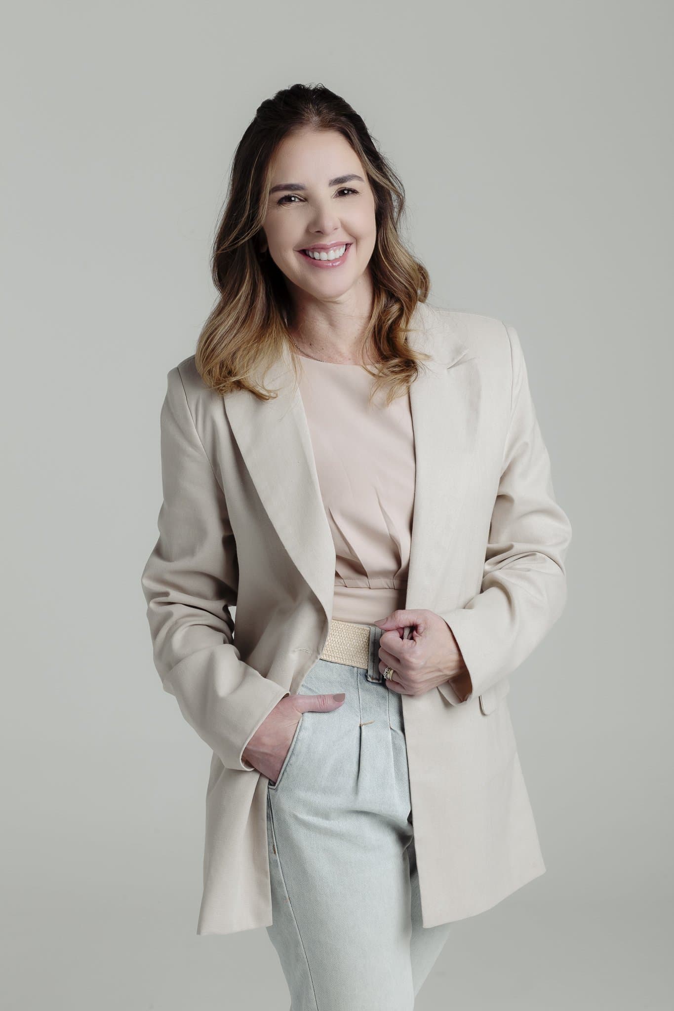 Anna Braga em pé, de blazer, sorrindo.