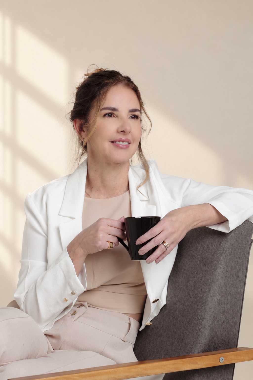 Anna Braga sentada, com uma xícara na mão, em conversa.